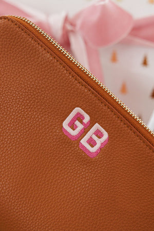 A tan leather pouch is embroidered with a pink shadow monogram.