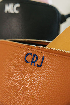 A tan leather pouch is customized with a navy embroidered monogram.