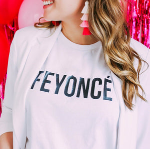 A woman wears a white t-shirt which reads "Feyonce" in a black, block font.