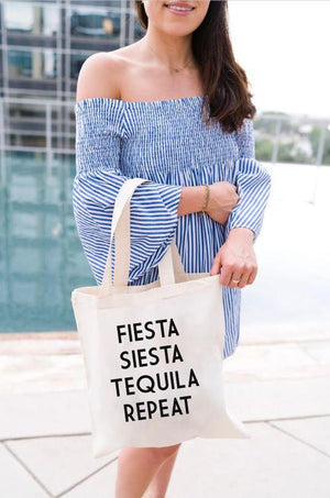 A woman stands at the pool holding her tote which says "Fiesta Siesta Tequila Repeat" in black.