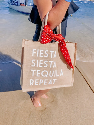 A woman on the beach holds a "Fiesta Siesta Tequila Repeat" Jute Tote 