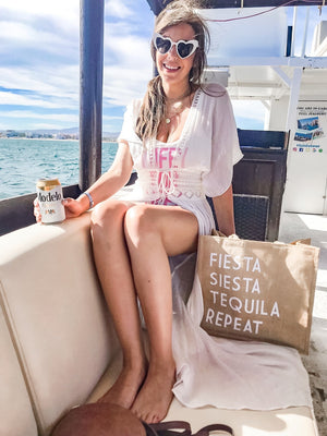 A woman on a boat sits with her "Fiesta Siesta Tequila Repeat" Jute Tote 