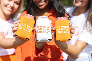 Three women dressed in orange hold their orange themed gameday can coolers
