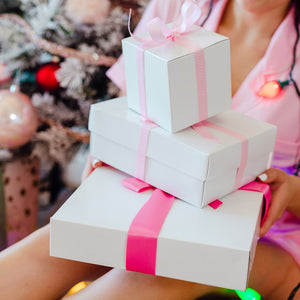 A person holds three white gift boxes wrapped in pink bows.