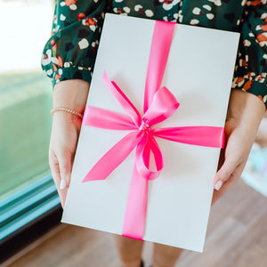 A woman holds a white gift box with a big pink bow
