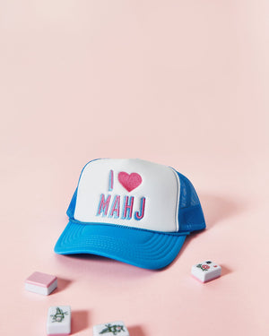 A white and blue trucker hat that reads "I <3 Mahjong" lays next to tiles