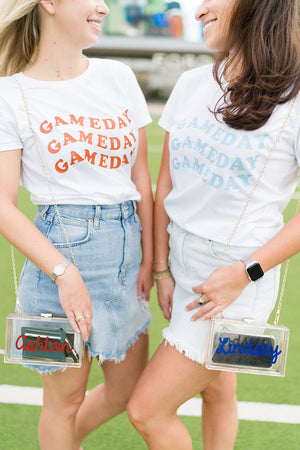 Two women sport custom game day shirts and personalized acrylic clutches.