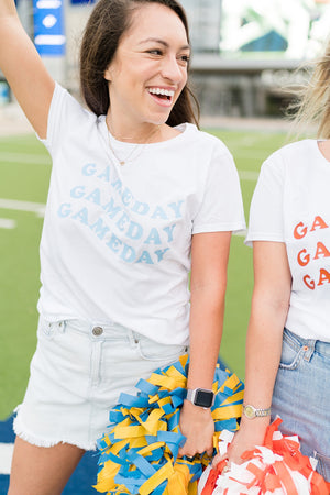A brunette wears a gameday shirt while holding blue and yellow pompoms.