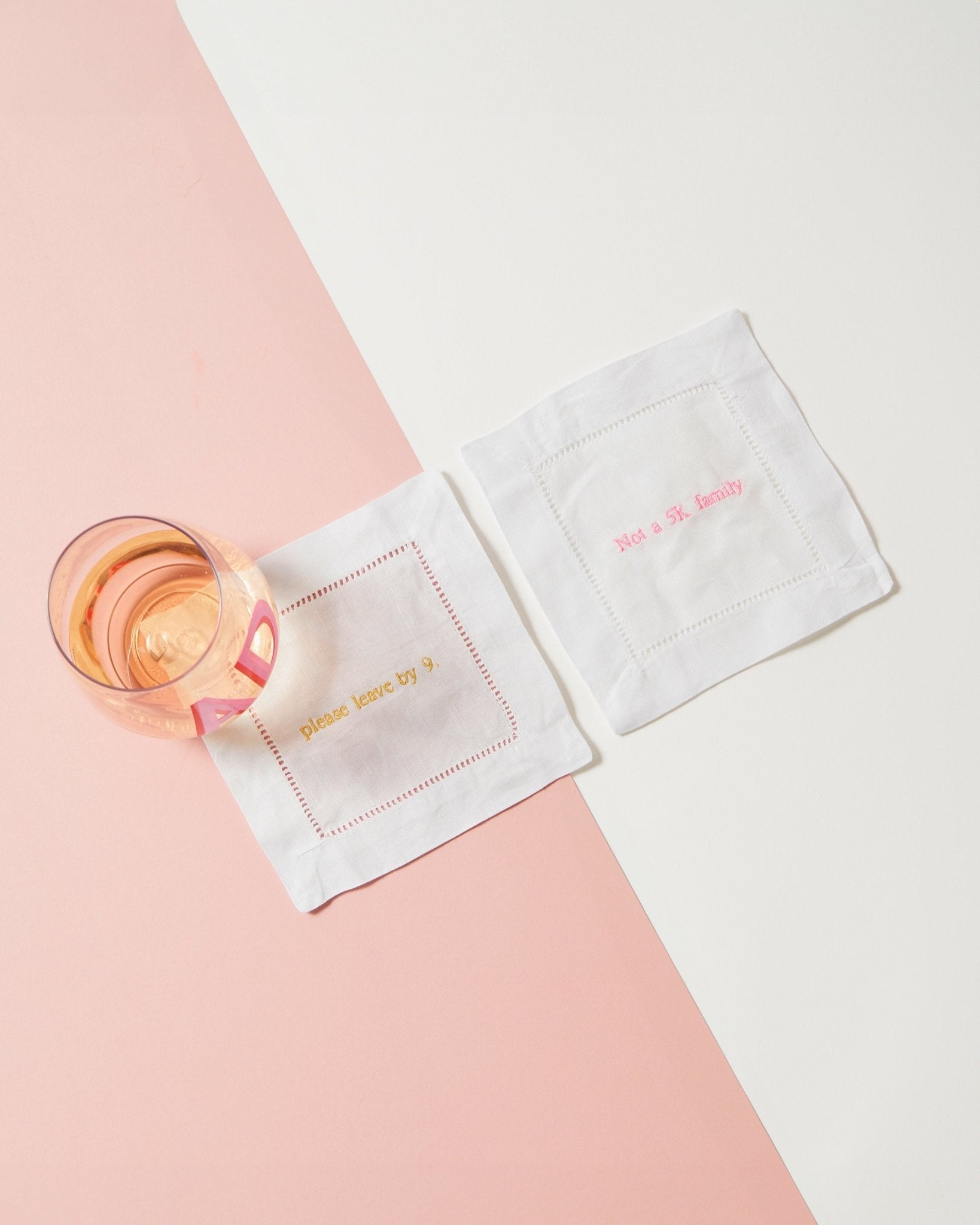 Two cocktail napkins customized with ironic phrases in pink and gold thread