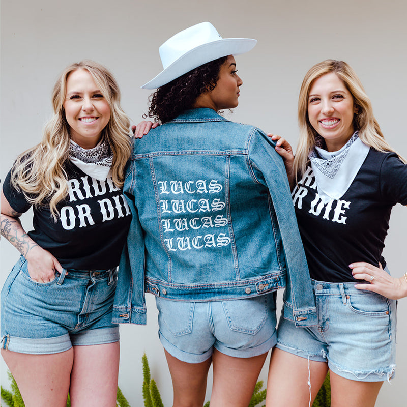 Two bridesmaid in western wear stand next to a bride wearing a custom denim jacket and cowboy hat.