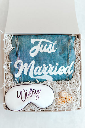 A box is put together for a bride featuring a denim jacket which reads "Just Married" and a sleep mask which says "Wifey."