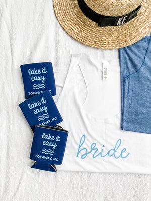 An assortment of products is laid out for a bachelorette including a "bride" shirt and navy koozie.