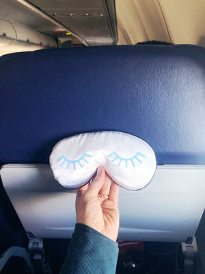 A person holds up a sleep mask with a light blue eyelash design on it.