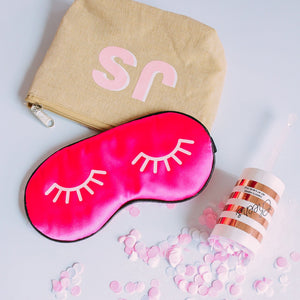 A bright pink sleep mask with a light pink eyelash design printed on it.