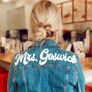 A woman shows off her custom retro denim jacket which reads "Mrs. Goswick" in white text across her shoulders.