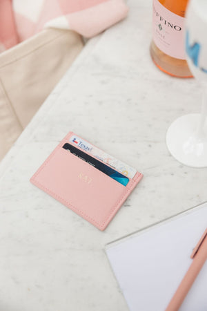 A pink, monogrammed card holder site on a table next to champagne