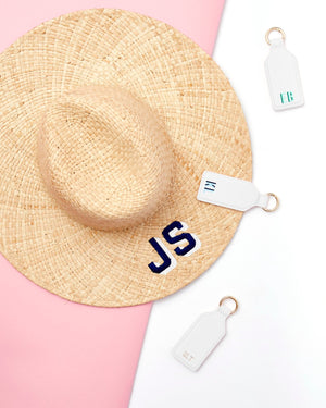 Three monogrammed white leather hat clips are placed around a straw hat