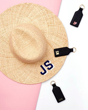Three monogrammed black leather hat clips are placed around a straw hat