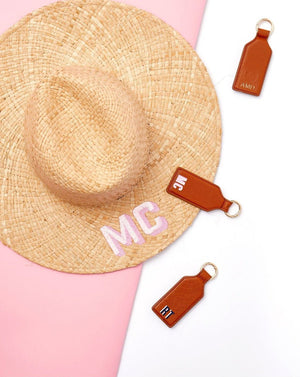Three monogrammed tan leather hat clips are placed around a straw hat