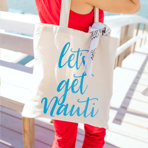 A woman holds a tote bag which reads "let's get nauti" in bright blue font.