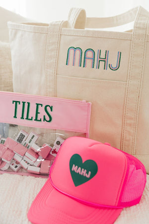 A collection of Mahjong themed items include a trucker hat, tile bag, and canvas tote