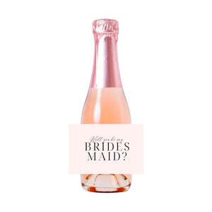 A champagne bottle is customized with a personalized label which says "Will You Be My Bridesmaid?"