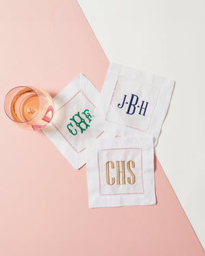 A wine glass sits on three embroidered cocktail napkins which are customized with different monograms and thread colors.