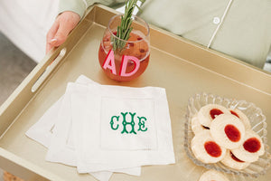 A woman holds up a tray with a customized wine glass and set of cocktail napkins with an embroidered monogram in a green thread color.