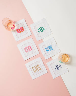 Six monogram cocktail napkins are set out with wine glasses to show off some of the embroidered monograms that can customize your cocktail napkins.