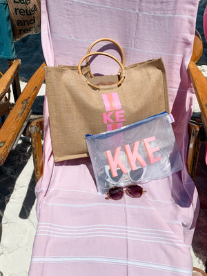 A jute tote and a white pool bag are monogrammed and placed on a beach chair