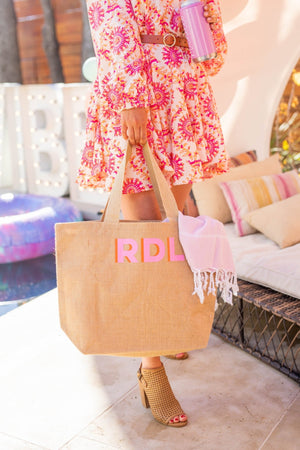 A woman in a pink and orange floral dress holds her personalized tote with a towel inside