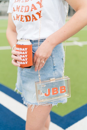 A woman holds a gameday can cooler and wears her stadium bag customized with her initials in orange and white.