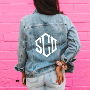 A woman wears a denim jacket with a white monogram on the back