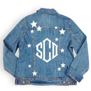 A denim jacket is customized with a diamond shaped monogram and stars in white.