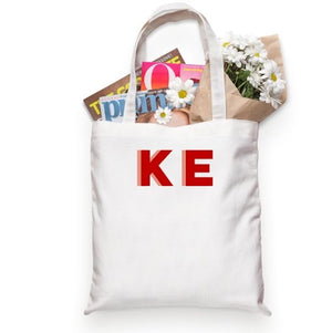 A tote bag is customized with initials in red and melon.