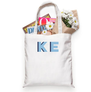 A tote bag is customized with initials in light blue and navy.