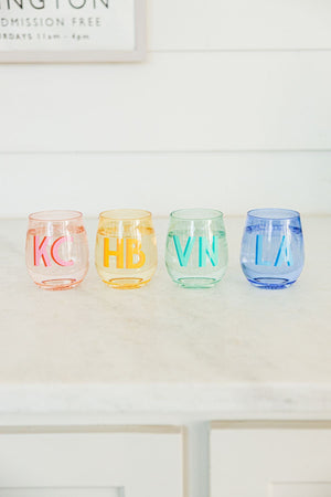 A pink, yellow, green, and a blue wine glass are personalized with different colored monograms.
