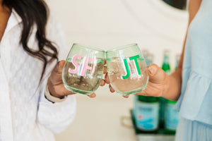 Two women cheers with their green monogrammed stemless wine glasses.