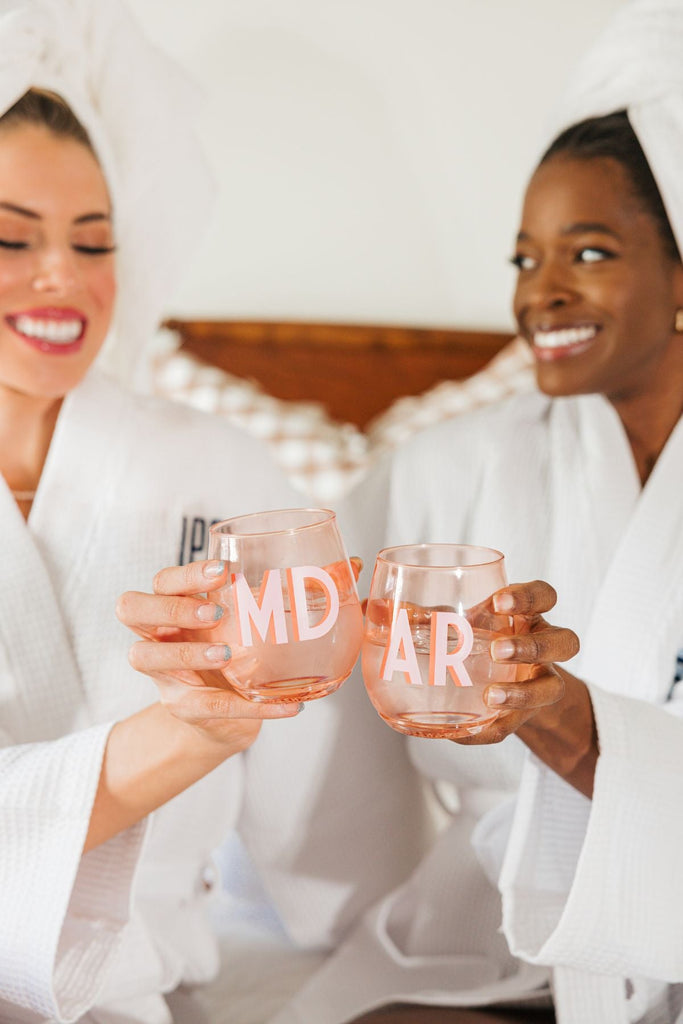 Two women cheers with their pink monogrammed stemless wine glasses.