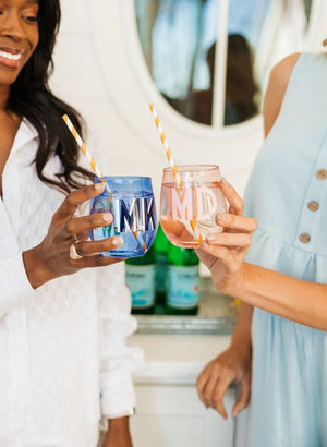 Two women cheers with their pink and blue monogrammed stemless wine glasses.