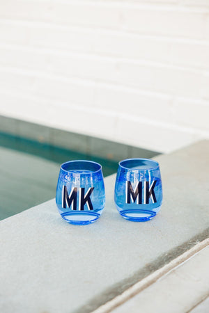 Two blue stemless wine glasses are customized with navy and white monograms.