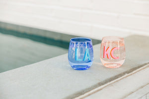 A blue and pink wine glass are customized with pink and blue monograms.