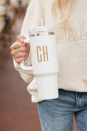 A blonde woman holds a white tumbler that reads "CH" in tan letters