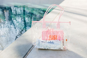 A pink clear tote is customized with a pink monogram and is filled with a towel and a pink pouch.