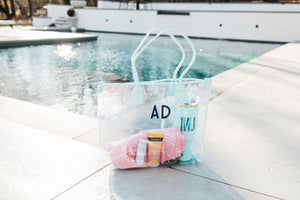 A blue clear tote is customized with a navy and white monogram and is filled with a towel and a blue tumbler.