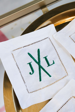 An embroidered cocktail napkin with skis and a custom monogram in green thread.