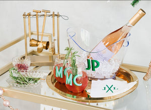 A bar cart is set up with accessories including monogrammed wine glasses, an ice bucket, and embroidered cocktail napkins with skis and a monogram.