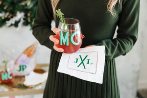 A woman holds a cocktail napkin under her drink that is embroidered with skis and a monogram in green thread.