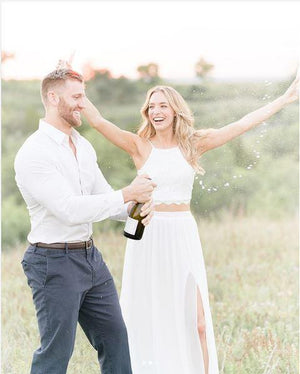A man and a woman in a field pop open a bottle of champagne in celebration.
