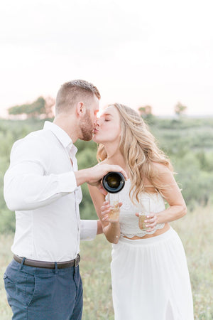 A couple kisses as they pour champagne into their customized flutes.